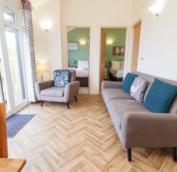 A living room with a sofa and armchair facing two bedrooms at Chalet Log Cabin L14 in Combe Martin