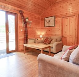 A living room with a wooden coffee table two beige sofas and curtains by a glass door at Chalet Lodge Bunks L1 in Combe Martin