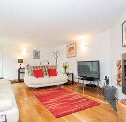 A living room with white sofas red cushions a red rug a flat screen tv and a fireplace at Great Brightor Cob Barn in St Kew Highway