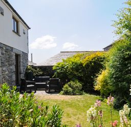 A garden with outdoor seating furniture and flowering plants next to a stone house at Great Brightor Cob Barn in St Kew Highway