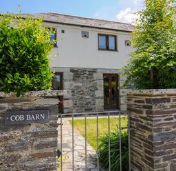 A stone gate with a metal gate leading to a house with stone and white walls at Great Brightor Cob Barn in St Kew Highway