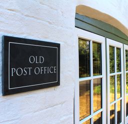 White wall with a black sign reading OLD POST OFFICE next to a window with multiple glass panes at Old Post Office Sherborne