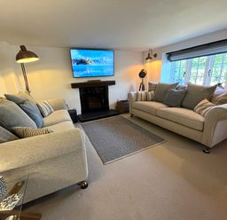 A living room with two sofas a TV above a fireplace and a window with blinds at Old Post Office in Sherborne