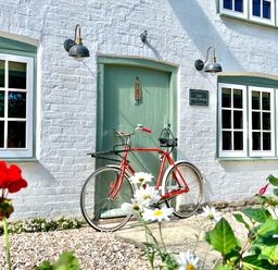 A red bicycle leaning against a green door on a white brick building with wall lights and flowers in the foreground at Old Post Office in Sherborne