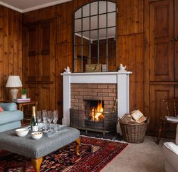 A living room with a fireplace wood-paneled walls sofas a coffee table and a basket of firewood at Flagstaff in Penmon near Beaumaris