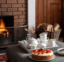 A table with a cake and a tea set near a fireplace with wood in a basket at Flagstaff in Penmon near Beaumaris