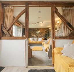 A living room with yellow and grey sofas stone walls and wooden beams at Mums Cottage Minions near Upton Cross