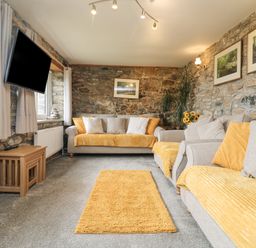 A living room with stone walls two sofas with yellow cushions and a yellow rug at Mum's Cottage Minions near Upton Cross
