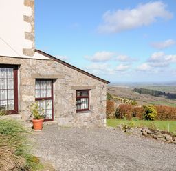 Exterior of a stone barn with windows and a potted plant overlooking a landscape with fields and bushes at Bickle Bice Cottage in Minions near Liskeard