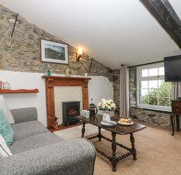 A living room with a grey sofa a fireplace and a wooden coffee table with flowers and snacks at Bickle Bice Cottage in Minions near Liskeard