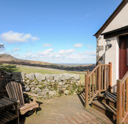A wooden deck with chairs and stairs leading to a door overlooking a stone wall and grassy hills at Cheesewring Cottage in Minions near Upton Cross