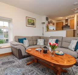 A living room with a gray sofa and a wooden coffee table with flowers and a coffee press at Cheesewring Cottage in Minions near Upton Cross