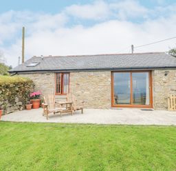 A stone cottage with wooden chairs on a patio and potted plants on grass at Fizz-Gog Cottage Minions near Upton Cross