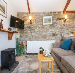 A living room with a stone wall a gray sofa blue cushions a wooden coffee table and a television at Fizz-Gog Cottage Minions near Upton Cross