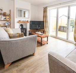 A living room with two sofas a wooden coffee table a television and sliding glass doors at 6 Cwrt Griffiths in Prestatyn