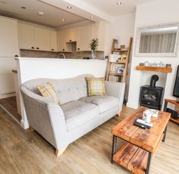 A living room with a gray sofa and wooden coffee table next to a fireplace and kitchen at 6 Cwrt Griffiths Prestatyn