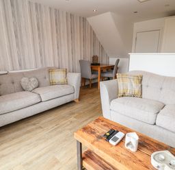 A living room with two gray sofas and a wooden coffee table with remotes and decorative items at 6 Cwrt Griffiths in Prestatyn
