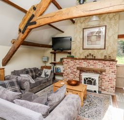 A living room with wooden beams sofas a brick fireplace and a television at The Cheese Loft in White Mill near Carmarthen