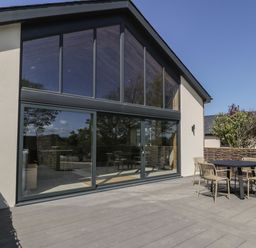 A patio with a round table and four chairs outside a building with large glass windows at The Barn in Llanfechell