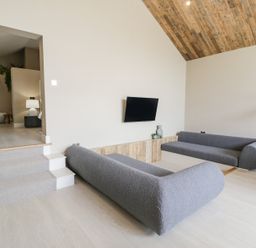 A living room with two gray sofas a wall mounted TV and wooden ceiling at The Barn in Llanfechell
