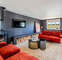 A living room with red sofas a wood burning stove and a television at Farmyard House in Llanfechell