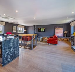 An open-plan living space with a kitchen island, red armchairs, a wall-mounted TV, and a wood-burning stove at Farmyard House in Llanfechell
