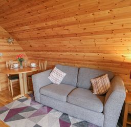 A living room with a gray sofa wooden dining table with chairs and a lamp on a side table at Pine Lodge in Llanddeusant near Llandovery