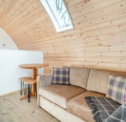 A curved wood-paneled room with a beige sofa and a small round wooden table with two stools at Carlton Manor Pod 2 in Aldbrough