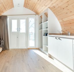 A small living area with a sofa a floor lamp kitchen cabinets and shelves near double doors at Carlton Manor Pod 2 in Aldbrough