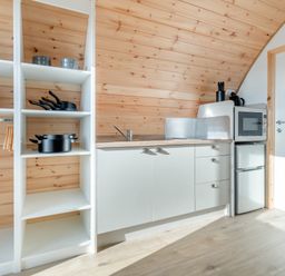 A kitchen with wooden walls white open shelves and cabinets with a microwave and mini fridge at Carlton Manor Pod 2 in Aldbrough