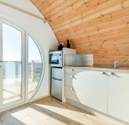 A small kitchen area with a microwave refrigerator and sink next to large circular glass doors at Carlton Manor Pod 8 in Aldbrough