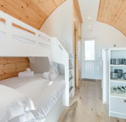 A bedroom with a white bunk bed wooden ceiling and shelves with kitchenware at Carlton Manor Pod 8 in Aldbrough