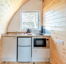 A compact kitchen with a sink, kettle, knives, refrigerator, and microwave beneath a window at Carlton Manor Pod 10 in Aldbrough