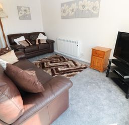 A sitting room with brown leather sofas a patterned rug a wooden cabinet a television on a stand and wall art at 39 Manorcombe Bungalows in Honicombe Holiday Village near Drakewalls