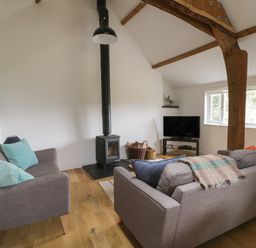 A living room with two gray sofas a black wood stove television on a stand and wooden beams at Brimley Barn in Kittisford near Milverton
