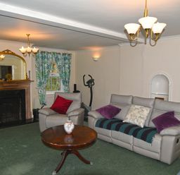 A living room with a fireplace armchair sofa round wooden table and exercise bike at Heathfield in Milverton