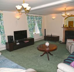 A living room with a round wooden coffee table and a television on a stand by the windows with green patterned curtains at Heathfield in Milverton