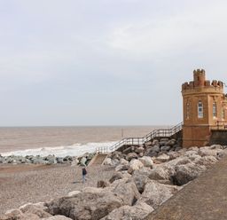 A pebble beach with large rocks and a small castle-like brick building by the sea at The Old Police House in Withernsea