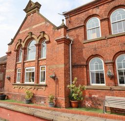 An exterior view of a red brick building with arched windows potted plants and a bench at The Old Police House in Withernsea