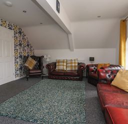 A living room with red leather sofas a chair yellow curtains and a floral wallpaper at The Old Police House in Withernsea