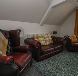 A sitting room with leather armchairs and a sofa with cushions and a window with curtains at The Old Police House in Withernsea