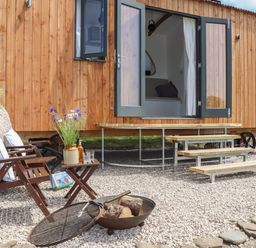 An outdoor seating area with two wooden chairs a small table with a vase of flowers near a wooden building with open double doors at Little Pip in Gulval