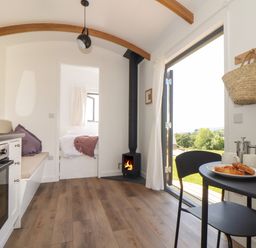 A small kitchen and dining area with a wood stove and an open door showing a garden at Little Pip in Gulval