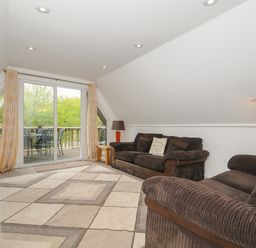 A living room with two brown sofas a patterned rug a floor lamp and sliding glass doors leading to a balcony at Valley Lodge 55 Callington near Gunnislake