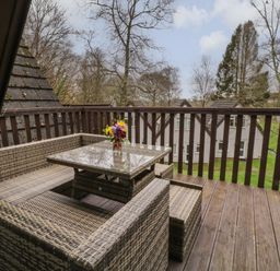 A balcony with a wicker seating set and glass table with flowers overlooking a grassy area at Valley Lodge 33 Callington near Gunnislake