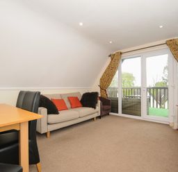 A living room with a beige sofa and red cushions near glass doors with yellow curtains at Valley Lodge 33 in Callington near Gunnislake