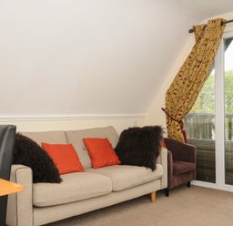 A living room with a beige sofa with red and dark brown cushions next to a sliding glass door with yellow patterned curtains at Valley Lodge 33 in Callington near Gunnislake