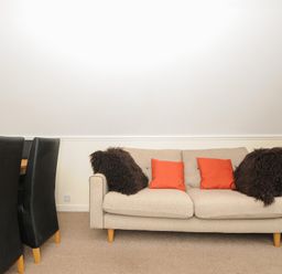 A beige sofa with red and dark brown pillows next to black dining chairs on a carpeted floor at Valley Lodge 33 in Callington near Gunnislake