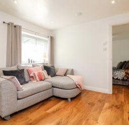 A living room with a gray sectional sofa and cushions by a window with beige curtains at Cosy Cottage in Broadwoodwidger near Lifton