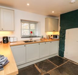 A kitchen with cream cabinets a wooden countertop a window above a double sink and a dark stone floor at Cosy Cottage Broadwoodwidger near Lifton